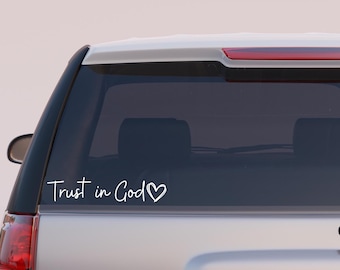 May include: A white decal on a car window with the words "Trust in God" in a handwritten font, followed by a heart symbol. The decal is placed on the rear window of a silver SUV.