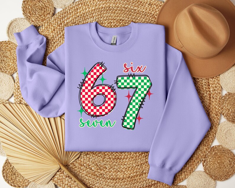 a purple sweatshirt with the number "67" and the text "seven" printed on it, along with a brown hat and a straw hat placed on a woven mat.