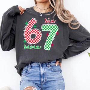 A woman wearing a gray sweatshirt with the number 67 and the text "Six seven" printed on it.