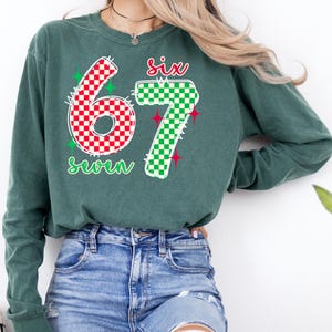 A woman wearing a green long-sleeved shirt with the number 67 and a patterned design, paired with distressed blue jeans.