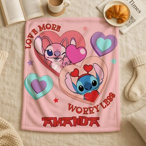 A pink blanket with a cartoon character design, featuring hearts and a message that says "Love More Worry Less".