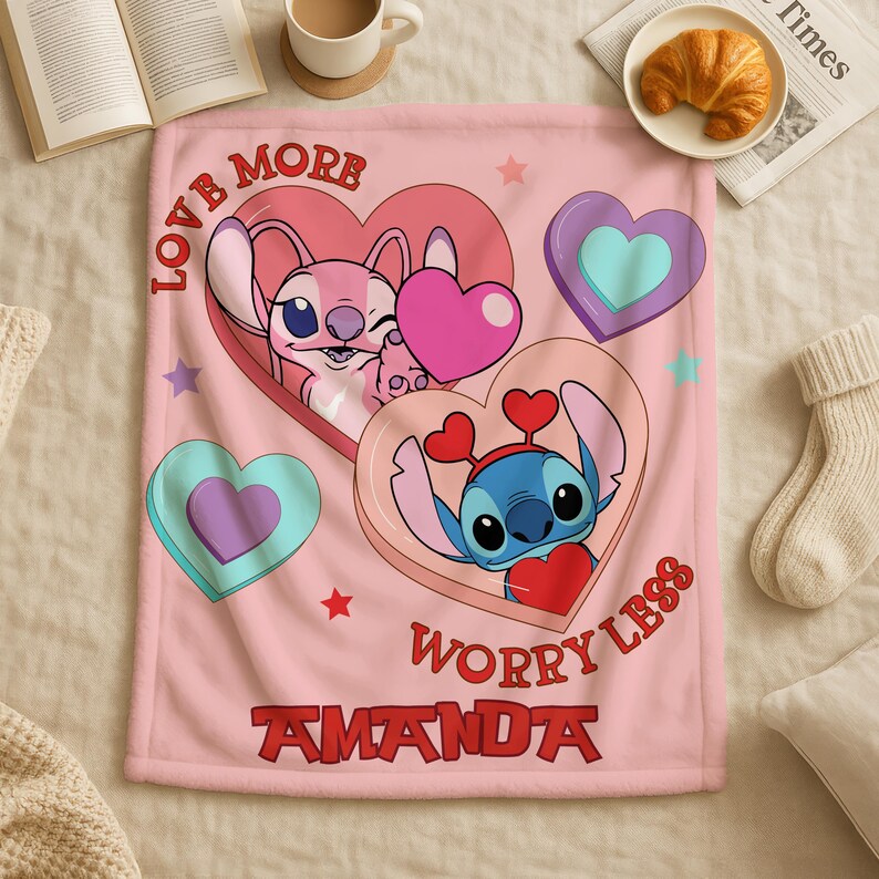 A pink blanket with a cartoon character design, featuring hearts and a message that says "Love More Worry Less".