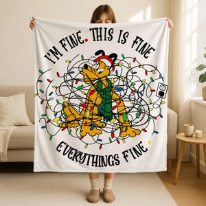 May include: White blanket with the phrase "I'M FINE. THIS IS FINE. EVERYTHING'S FINE" in black text. The blanket features a cartoon dog tangled in Christmas lights, wearing a Santa hat and green scarf. A plug is also visible.