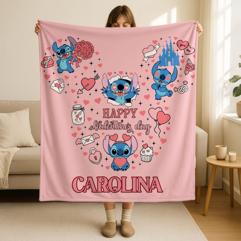 A person is holding up a pink blanket with various cartoon characters and illustrations, including a character named Carolina.