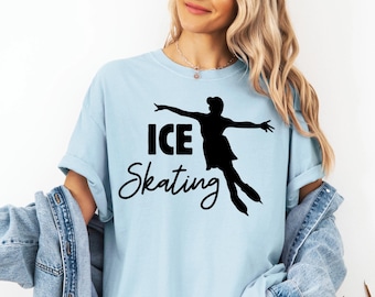 May include: Light blue t-shirt with a black silhouette of an ice skater and the words "ICE Skating" in a bold, black font. The skater is in mid-air with arms outstretched. The shirt is a casual style.