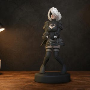 以下が含まれることがあります： 短い白髪で黒い目隠しをしたキャラクターの立ち姿のフィギュア。パフスリーブの黒いドレス、柄入りのスカート、太ももまでの黒いブーツを着用しており、円形の黒い台座の上に固定されている。