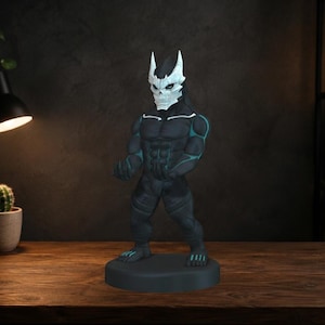 May include: A standing figurine of a muscular character with a dark grey body, teal accents on the chest and limbs, and a white, jagged, skull-like mask. The figure is posed with arms slightly bent and stands on a circular dark grey base.