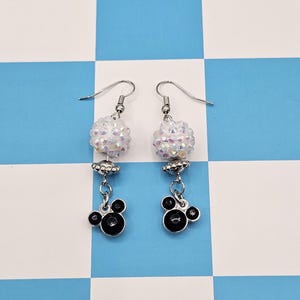 May include: A pair of dangle earrings with a whimsical design. Each earring features a cluster of iridescent beads, a silver-toned charm, and a black Mickey Mouse-shaped charm. The earrings hang from silver-colored fish hook ear wires.