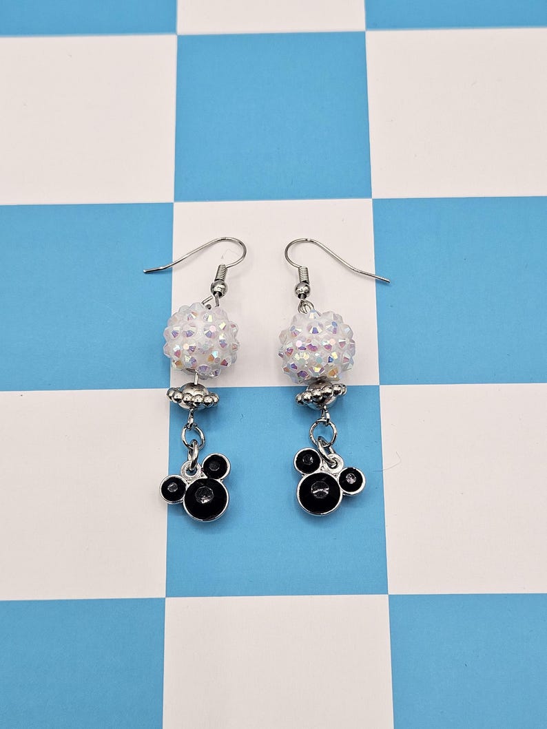 May include: A pair of dangle earrings with a whimsical design. Each earring features a cluster of iridescent beads, a silver-toned charm, and a black Mickey Mouse-shaped charm. The earrings hang from silver-colored fish hook ear wires.