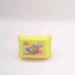 May include: A yellow package of "Scribblers" shaped like a popsicle. The package has the words "Popsicle" and "Scribblers" in blue and red, with a drawing of pencils. The word "Shopkins" is also visible.