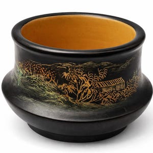 May include: Black ceramic bowl with a landscape design in gold and green. The interior of the bowl is a warm yellow color. The bowl has a rounded base and a wide opening.