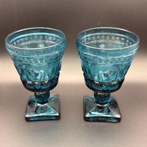 May include: A white ceramic mug with a black handle and the text "But First, Coffee" in a black, handwritten-style font. The mug is on a white surface.