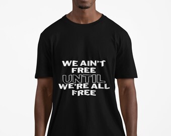 以下が含まれることがあります： 白い文字で「WE AIN'T FREE UNTIL WE'RE ALL FREE」と書かれた黒いTシャツ。Tシャツは半袖で、人が着ています。その人はチェック柄のズボンを履いています。