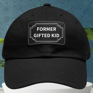 Può includere: Cappellino da baseball nero con visiera curva. Una toppa rettangolare sul davanti mostra la scritta "FORMER GIFTED KID" in lettere bianche su sfondo nero, incorniciata da un bordo bianco. Il cappellino è realizzato in tessuto morbido.