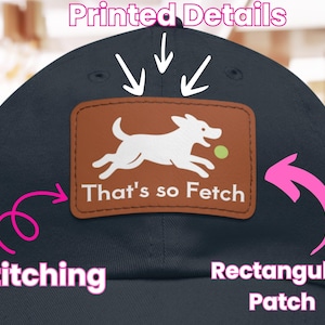 Puede incluir: Gorra de béisbol azul marino con un parche rectangular marrón. El parche muestra un perro blanco persiguiendo una pelota verde y el texto "That's so Fetch". Detalles de costura.