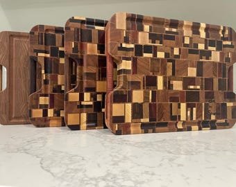 May include: A collection of wooden cutting boards with various geometric patterns. The boards are made of different wood types, creating a mosaic-like design with shades of brown, red, and tan. One board has a handle, and the others have curved edges.