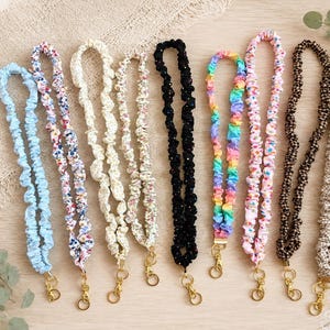 May include: A collection of nine fabric lanyards featuring various patterns and colors, including solid light blue, floral prints, black with white dots, rainbow stripes, pink with colorful dots, and brown and beige checkered designs with gold clasps.