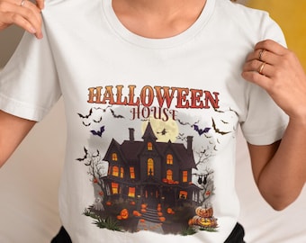 May include: White t-shirt featuring a Halloween design. The graphic includes a spooky house, pumpkins, bats, and the words "Halloween House" in orange and red lettering. A full moon is in the background.
