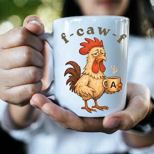 Può includere: Tazza in ceramica bianca con un disegno di gallo dei cartoni animati. La tazza presenta la scritta "f-caw-f" e un gallo che tiene in mano una tazza di caffè con la lettera "A". Il gallo è raffigurato in marrone, rosso e giallo, con un'espressione stanca.