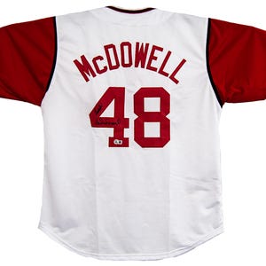 May include: White baseball jersey with red sleeves. The back features the name "McDowell" above the number "48" in red. Includes a signature. A classic sports apparel item.