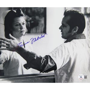 May include: Black and white photograph featuring two people, one with their hands outstretched. The image is signed in blue ink. The photograph appears to be a still from a film or television show.