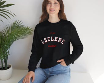 Könnte beinhalten: Schwarzes Sweatshirt mit Rundhalsausschnitt und dem Text "LECLERC ACADEMY" in weißer und roter Schrift. Das Sweatshirt hat auch den Text "EST 1853" über dem Haupttext. Das Sweatshirt wird von einer Person getragen.