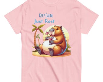 Puede incluir: Camiseta rosa claro con un dibujo de un carpincho relajándose en una playa, sosteniendo un cóctel con una pequeña sombrilla. El texto "Keep Calm Just Rest" está encima del carpincho. El diseño incluye una palmera y una puesta de sol.