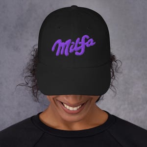 May include: Black baseball cap with the word "Milfsa" embroidered in purple script across the front. The cap has a curved brim and a structured fit. The hat is worn by a person.