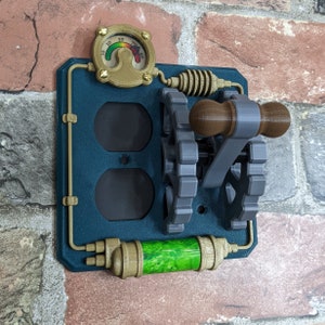 May include: A teal blue wall plate with a steampunk design. It features a toggle switch with a wooden handle, two electrical outlets, a gauge with a green and red needle, and a gold pipe with a green liquid.