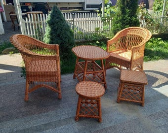 May include: A set of outdoor wicker furniture, including two armchairs, a small round table, a small square table, and a round stool. The furniture is made of woven brown wicker.