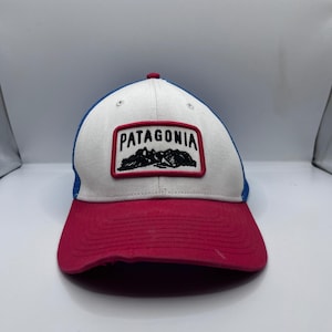 May include: A red, white, and blue baseball cap with the word "PATAGONIA" embroidered on the front. The cap features a mountain graphic and a red peak. A classic style cap.