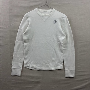 May include: A white long-sleeve thermal shirt with a crew neckline and a ribbed collar. The shirt features a small dark embroidered logo on the upper left chest with the letters A&F. It has a triangular ribbed detail below the neckline.