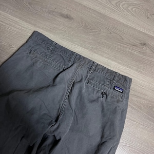 Puede incluir: Pantalones grises Patagonia con cierre de botón y bolsillos traseros. El logotipo de Patagonia es visible en el bolsillo trasero. Los pantalones están hechos de un material duradero y parecen usados.