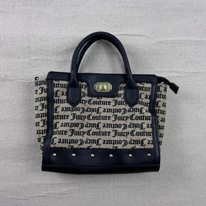 Puede incluir: Bolso tote negro y beige con asas y ribetes negros. El bolso presenta las palabras "Juicy Couture" en un patrón repetido. El bolso tiene un cierre dorado y tachuelas plateadas en la parte inferior.