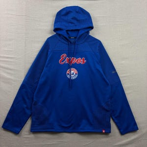 May include: A royal blue long-sleeve hooded sweatshirt featuring the red text Expos across the chest. Below the text is a circular logo with the words Exposure Baseball in white and red. The hoodie includes a drawstring and textured panels.