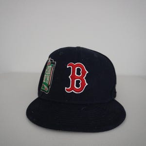Può includere: Un cappellino da baseball blu navy con una lettera B rossa ricamata sul davanti. Sul lato, una toppa con dettagli verdi, bianchi e rossi riporta la scritta All Star Game 99. Il cappellino presenta una visiera piatta e una corona strutturata.