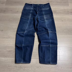 May include: Dark blue denim jeans with a distinctive patchwork design. These high-waisted, wide-leg jeans feature visible stitching that outlines geometric panels. The denim has a faded appearance, enhancing the vintage aesthetic.