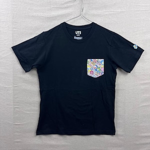 Könnte beinhalten: Ein schwarzes Kurzarm-T-Shirt mit einer Brusttasche, die mit einem bunten Blumen- und Figuren-Print versehen ist. Das T-Shirt hat einen Rundhalsausschnitt, das UT-Logo im Innenkragen und ein kleines Blumenemblem am linken Ärmelrand.
