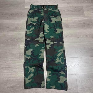 May include: Camouflage-patterned pants in shades of green, brown, and black. The pants have a button and zipper closure, along with pockets. The fabric appears to be a durable material, suitable for outdoor activities or casual wear.