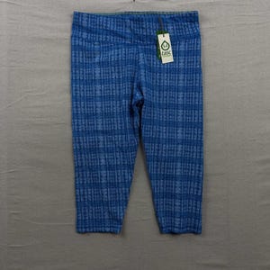 May include: Blue cropped leggings featuring a repeating geometric grid pattern in varying shades of blue. The garment has an elastic waistband and includes a white rectangular tag attached to the front with the green tasc organic logo text.