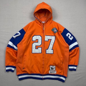 Peut inclure: Sweat à capuche orange zippé avec le numéro 27 blanc sur le devant. Les manches ont des accents bleus et blancs avec le numéro 27. Un écusson est sur le haut de la poitrine gauche. Le bas et les poignets ont des rayures bleues et blanches.