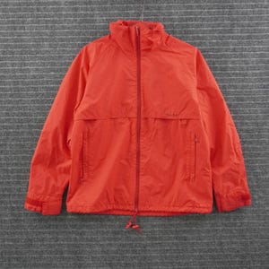 May include: A bright orange windbreaker jacket featuring a full-length front zipper, a high collar, and long sleeves with adjustable hook-and-loop cuffs. The jacket includes two vertical zippered side pockets and a drawstring hem at the waist.