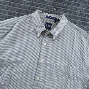 Op de afbeelding: Een overhemd met lange mouwen en knoopsluiting met een klein blauw en wit ruitpatroon. Het overhemd heeft een button-down kraag, een borstzak en een blauw label bij de nek met de tekst GAP en The Big Oxford in witte letters.
