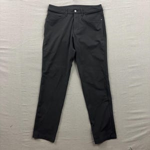 Op de afbeelding: Zwarte broek met knoopsluiting en zakken. De broek is gemaakt van een gladde, donkere stof en heeft een klassiek, rechtbenig ontwerp. De broek ligt plat op een neutrale ondergrond.