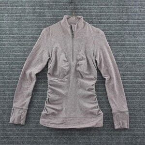 May include: A heathered mauve long-sleeve athletic top featuring a mock neck with a front zipper closure, vertical ruched detailing along the torso, and integrated thumbholes at the cuffs of the sleeves, presented on a hanger.