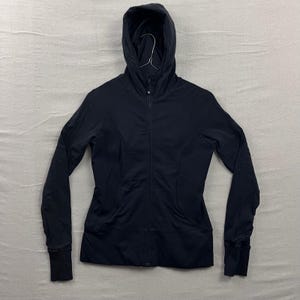 May include: A black hooded jacket with a full-length zipper. The jacket has long sleeves with ribbed cuffs and a fitted silhouette. The hood is attached and has a drawstring. The jacket is made of a lightweight, athletic material.