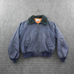 May include: A navy blue bomber jacket featuring a dark green faux fur collar, a full-length front zipper, and two front flap pockets with button closures. The interior lining is bright orange, and the cuffs and hem are made of ribbed fabric.