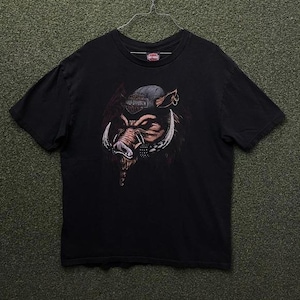 May include: Black t-shirt featuring a graphic of a wild boar wearing a cap and a studded collar. The boar graphic has large tusks and a Harley-Davidson logo on the cap. The shirt is hanging on a metal hanger.