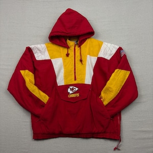 May include: Red, yellow, and white hooded pullover jacket. The jacket features a front pocket, a half-zip closure, and the Kansas City Chiefs logo on the chest. The sleeves have yellow accents, and the hood is red.