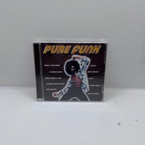 May include: A CD case with the title "Pure Funk" in gold lettering. The cover features a stylized image of a man with an afro and a patterned jacket. The names of various artists are listed on the left and right sides.